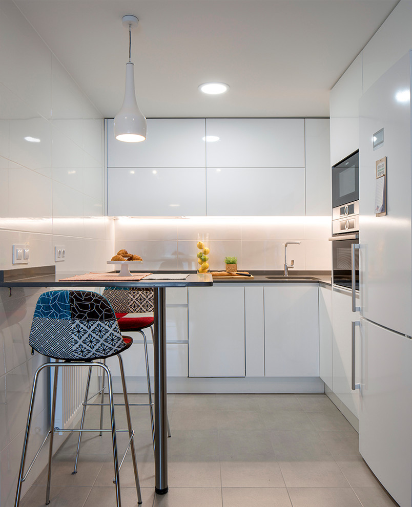 Moderne Küche in L-Form mit Unterbauwaschbecken, flächenbündigen Schrankfronten, weißen Schränken, Küchenrückwand in Weiß, weißen Elektrogeräten und beigem Boden in Bilbao