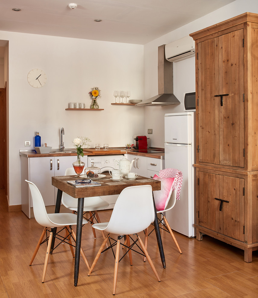 Inspiration for a small farmhouse l-shaped kitchen/diner in Malaga with flat-panel cabinets, white cabinets, wood worktops, white splashback, white appliances, medium hardwood flooring and no island.