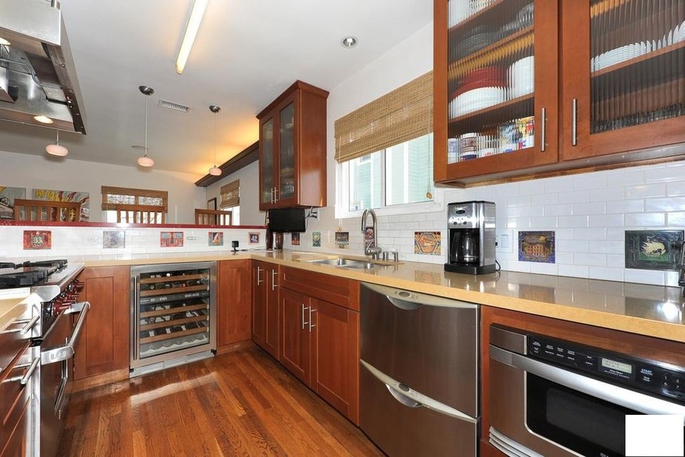 Exempel på ett mellanstort modernt beige linjärt beige kök och matrum, med en dubbel diskho, luckor med glaspanel, bruna skåp, granitbänkskiva, vitt stänkskydd, stänkskydd i tunnelbanekakel, rostfria vitvaror, plywoodgolv och brunt golv