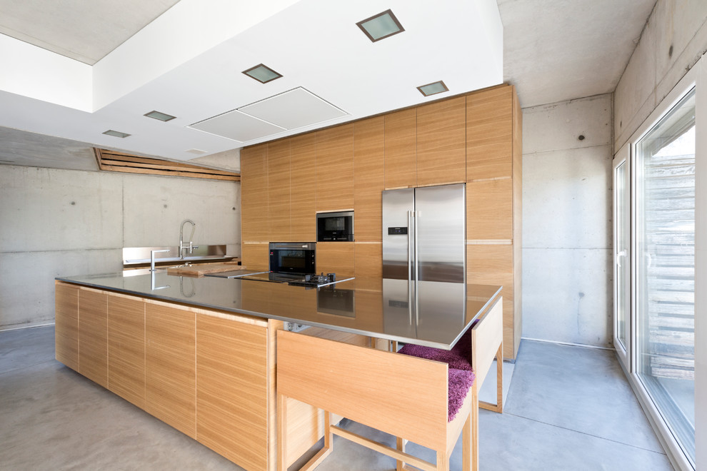 Photo of a large kitchen in London with an integrated sink, flat-panel cabinets, brown cabinets, stainless steel worktops, stainless steel appliances, concrete flooring and an island.