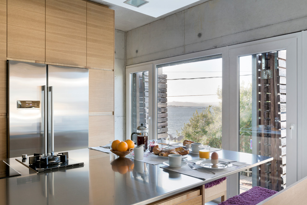 Large kitchen in London with an integrated sink, flat-panel cabinets, medium wood cabinets, stainless steel worktops, stainless steel appliances, concrete flooring and a breakfast bar.