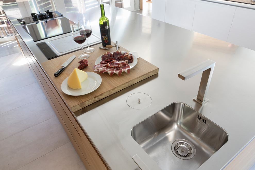 This is an example of a large contemporary open plan kitchen in London with an integrated sink, flat-panel cabinets, brown cabinets, stainless steel worktops, stainless steel appliances, concrete flooring and an island.