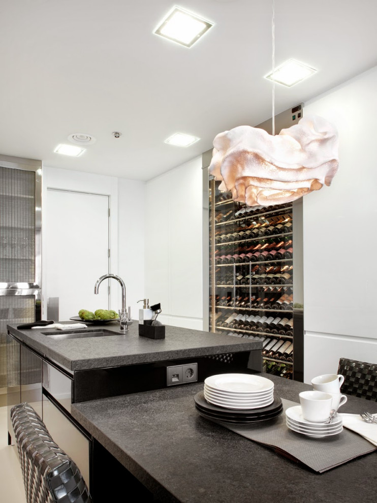 Große Moderne Küche in U-Form mit Unterbauwaschbecken, flächenbündigen Schrankfronten, weißen Schränken, Elektrogeräten mit Frontblende, Kücheninsel, grauem Boden und schwarzer Arbeitsplatte in Barcelona