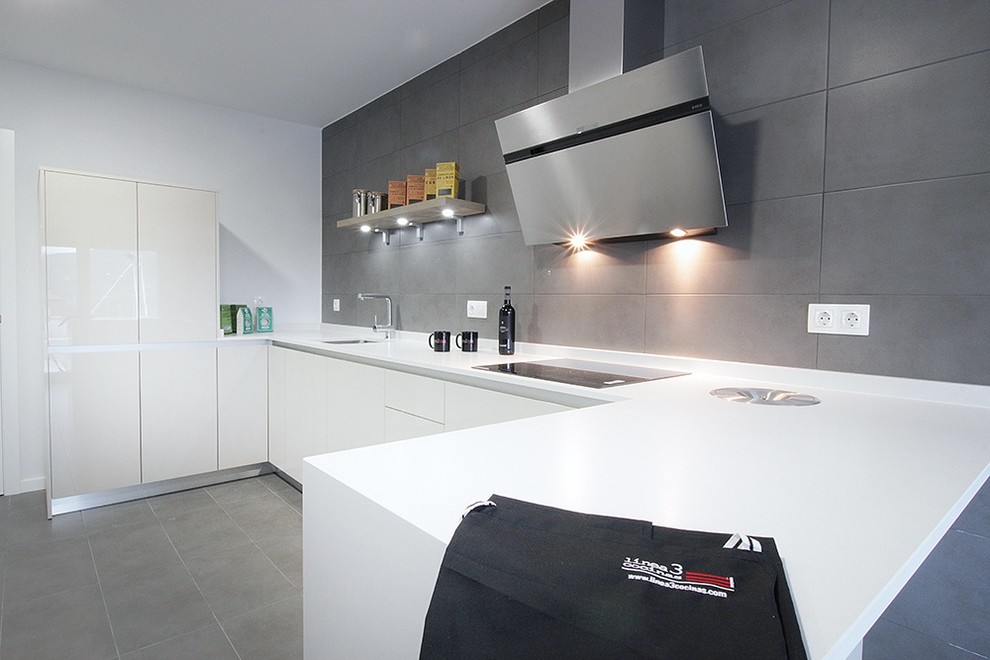 This is an example of a medium sized contemporary u-shaped kitchen/diner in Madrid with a submerged sink, flat-panel cabinets, white cabinets, engineered stone countertops, white splashback, stainless steel appliances and ceramic flooring.