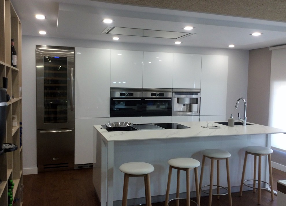 Immagine di una grande cucina minimalista con lavello sottopiano, ante lisce, ante bianche, elettrodomestici in acciaio inossidabile e pavimento in legno massello medio