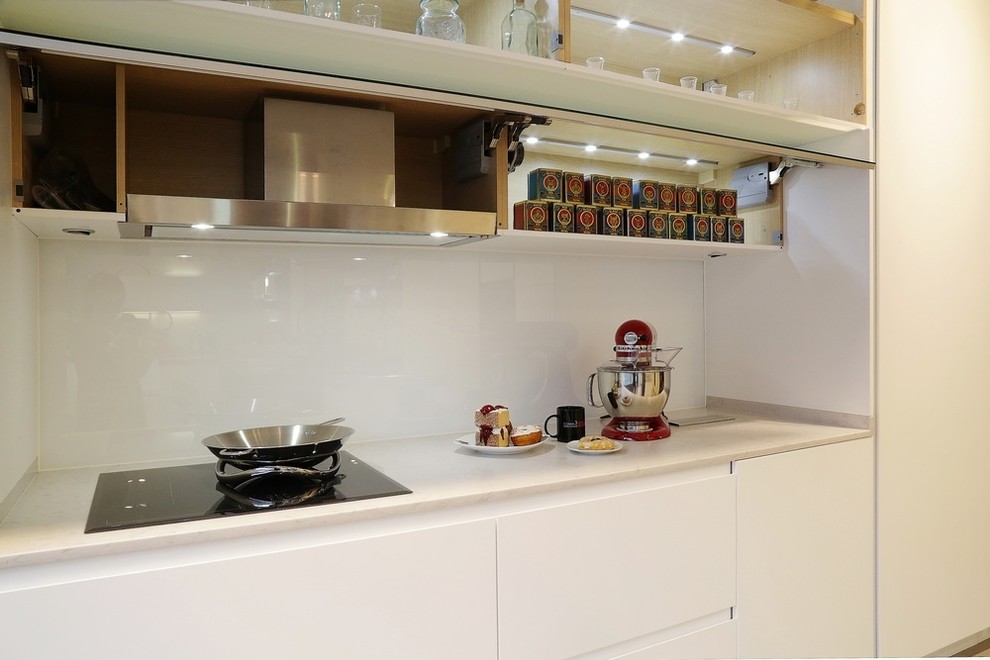 Ejemplo de cocina lineal actual abierta con armarios con paneles lisos, puertas de armario blancas, encimera de cuarcita, salpicadero blanco, salpicadero de vidrio templado, suelo vinílico y una isla