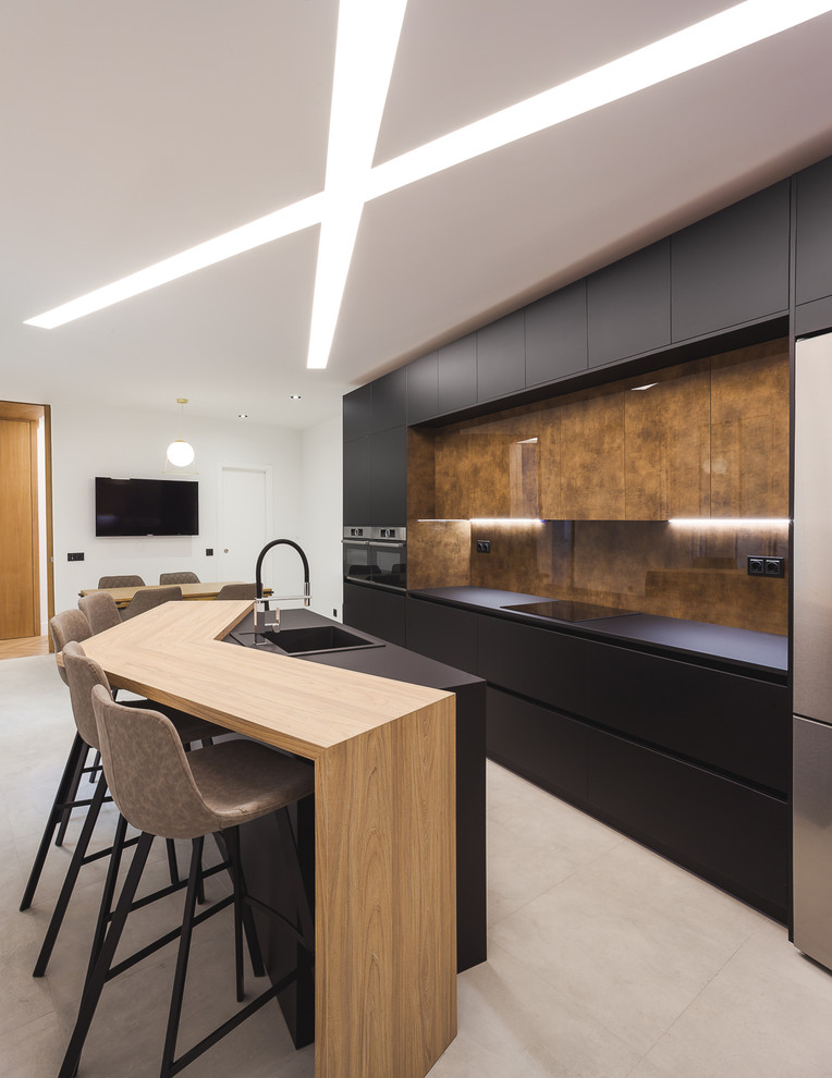 This is an example of a contemporary galley kitchen/diner in Madrid with a built-in sink, flat-panel cabinets, black cabinets, brown splashback, stainless steel appliances, an island, grey floors and black worktops.