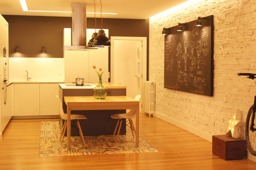 Medium sized urban l-shaped kitchen/diner in Bilbao with flat-panel cabinets, white cabinets, integrated appliances, medium hardwood flooring, an island and a submerged sink.