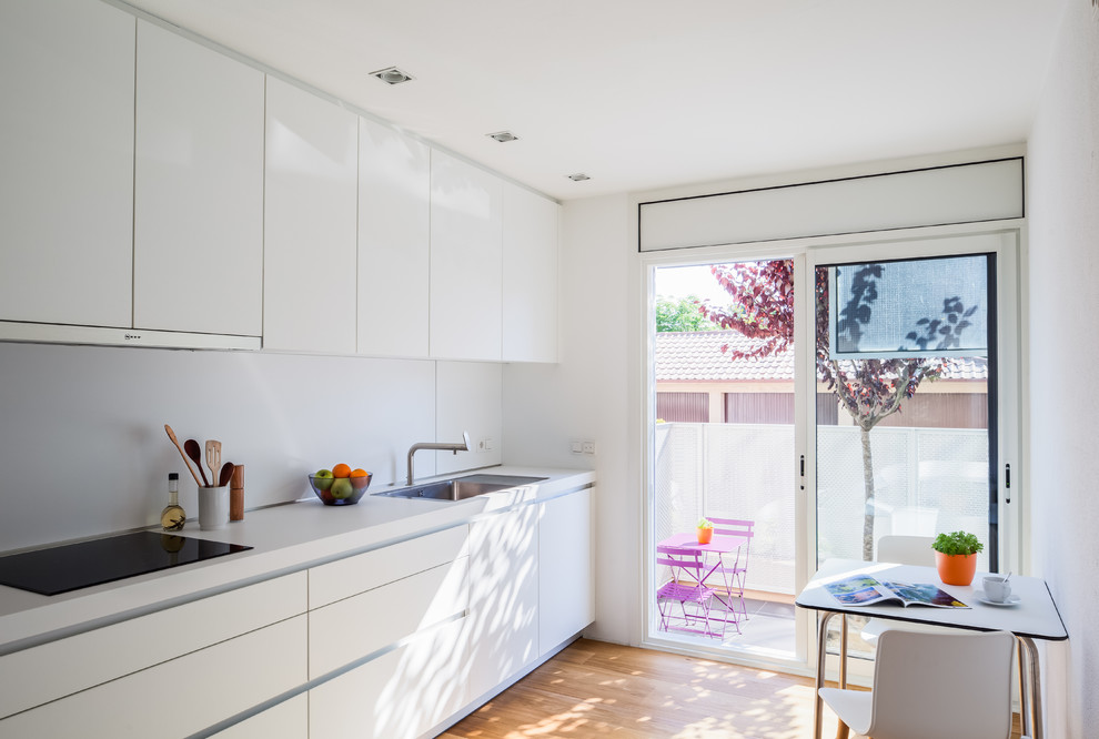 Réalisation d'une cuisine ouverte design en L avec un évier 1 bac, un placard à porte plane, des portes de placard blanches, un plan de travail en stratifié, une crédence blanche, un électroménager en acier inoxydable, un sol en bois brun, aucun îlot et un sol marron.