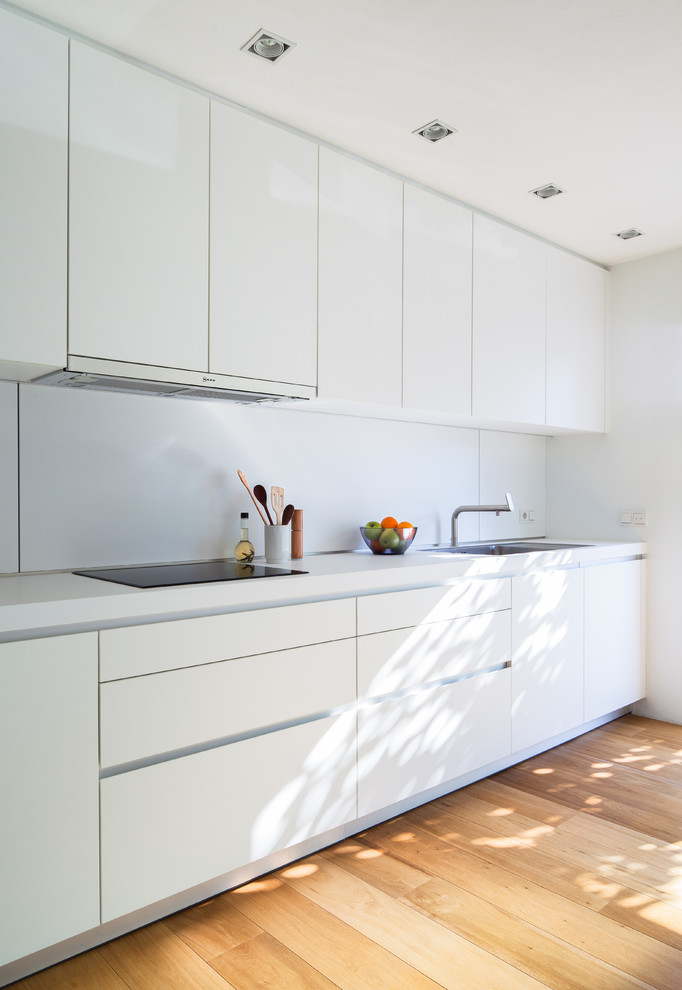 Foto på ett mellanstort funkis linjärt kök med öppen planlösning, med släta luckor, vita skåp, vitt stänkskydd, mellanmörkt trägolv, rostfria vitvaror, en enkel diskho, laminatbänkskiva och brunt golv