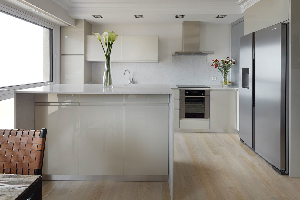 Esempio di una cucina abitabile design con ante lisce, ante beige, paraspruzzi grigio, elettrodomestici in acciaio inossidabile, parquet chiaro, pavimento beige e top bianco