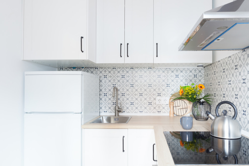 Example of a small danish l-shaped ceramic tile and gray floor open concept kitchen design in Madrid with a drop-in sink, beaded inset cabinets, white cabinets, laminate countertops, gray backsplash, ceramic backsplash, white appliances, no island and brown countertops