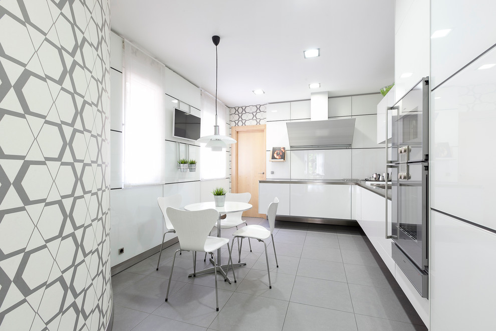 Mittelgroße Moderne Wohnküche ohne Insel in L-Form mit flächenbündigen Schrankfronten, weißen Schränken, Küchengeräten aus Edelstahl, Keramikboden und Küchenrückwand in Weiß in Madrid