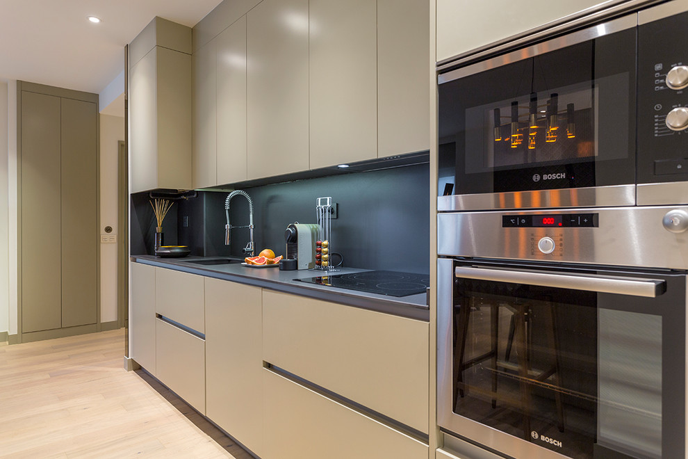 This is an example of a medium sized contemporary l-shaped open plan kitchen in Madrid with an integrated sink, flat-panel cabinets, beige cabinets, engineered stone countertops, black splashback, stainless steel appliances, light hardwood flooring and beige floors.