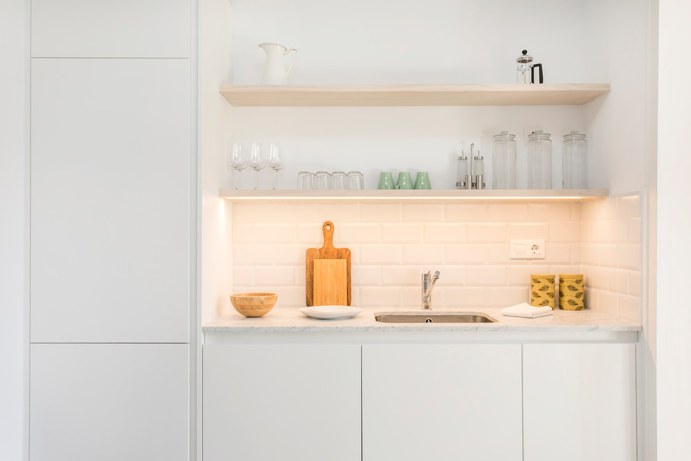 Inredning av ett modernt litet linjärt kök, med en undermonterad diskho, släta luckor, vita skåp, marmorbänkskiva, vitt stänkskydd, stänkskydd i tunnelbanekakel och integrerade vitvaror