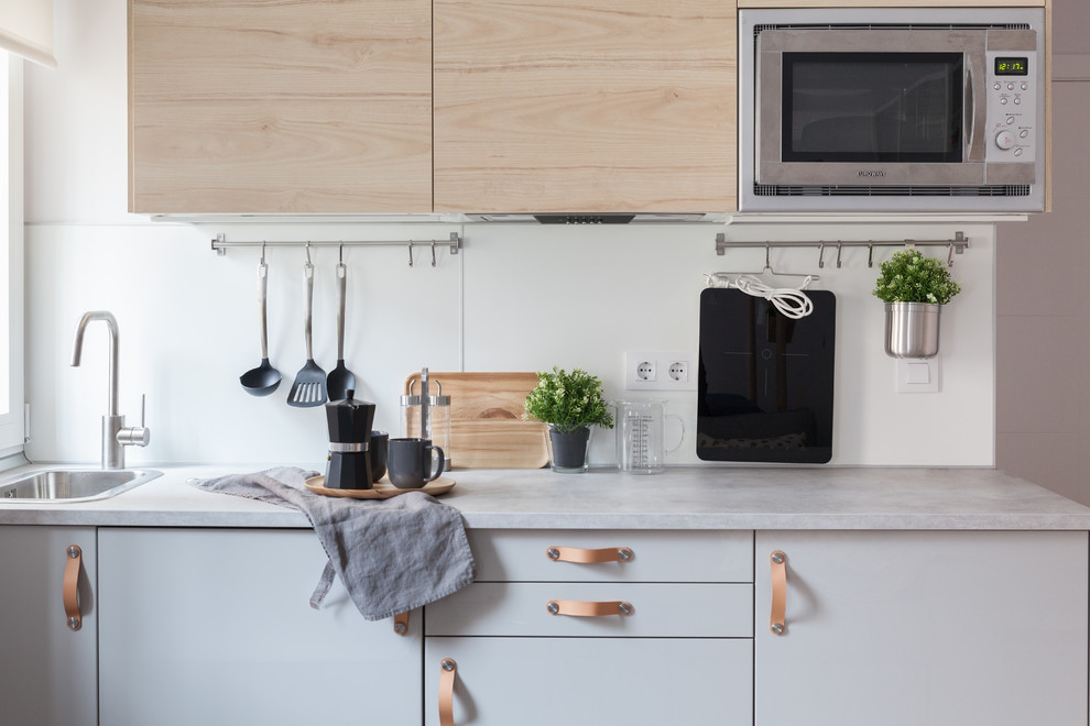 Idée de décoration pour une petite cuisine ouverte linéaire nordique en bois clair avec un évier posé, un placard à porte plane, un plan de travail en stratifié, une crédence blanche, fenêtre, un électroménager en acier inoxydable, sol en stratifié, aucun îlot, un sol marron et un plan de travail gris.