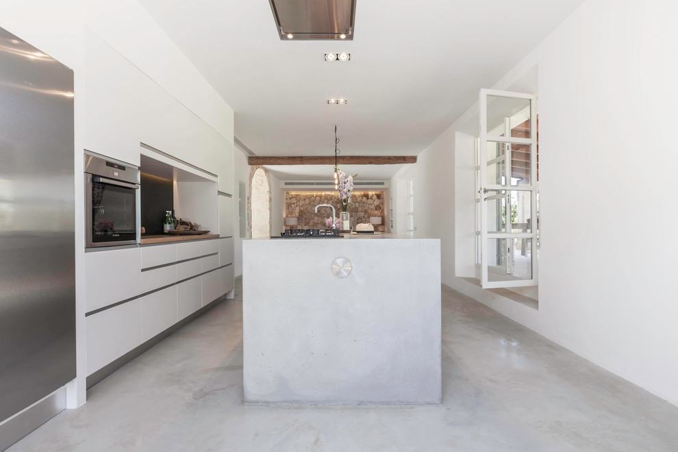 Ejemplo de cocina lineal mediterránea de tamaño medio abierta con armarios con paneles lisos, puertas de armario blancas, electrodomésticos de acero inoxidable y una isla