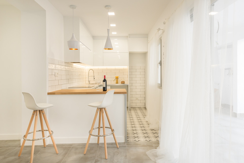 На фото: маленькая п-образная кухня-гостиная в скандинавском стиле с плоскими фасадами, белыми фасадами, деревянной столешницей, полом из керамической плитки и полуостровом для на участке и в саду