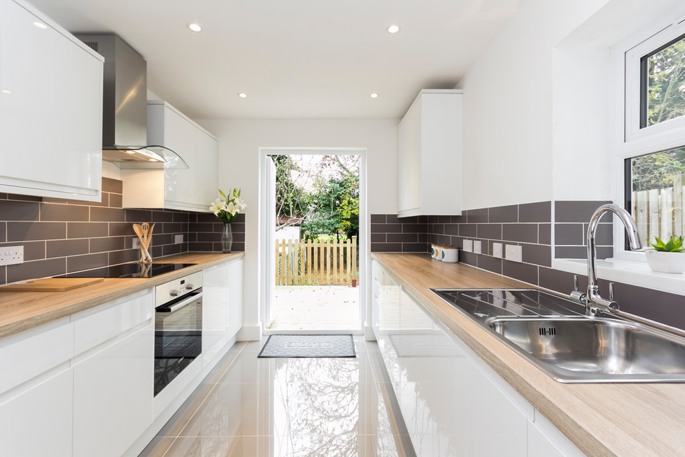 Contemporary single-wall kitchen in Madrid with a belfast sink, flat-panel cabinets, white cabinets, wood worktops, grey splashback and stainless steel appliances.