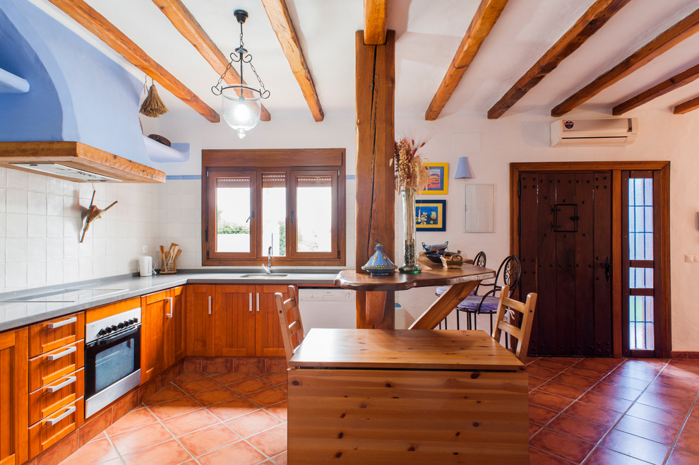 Immagine di una cucina a L mediterranea con ante con riquadro incassato, ante in legno scuro, paraspruzzi bianco, elettrodomestici bianchi, penisola, pavimento rosso e top grigio