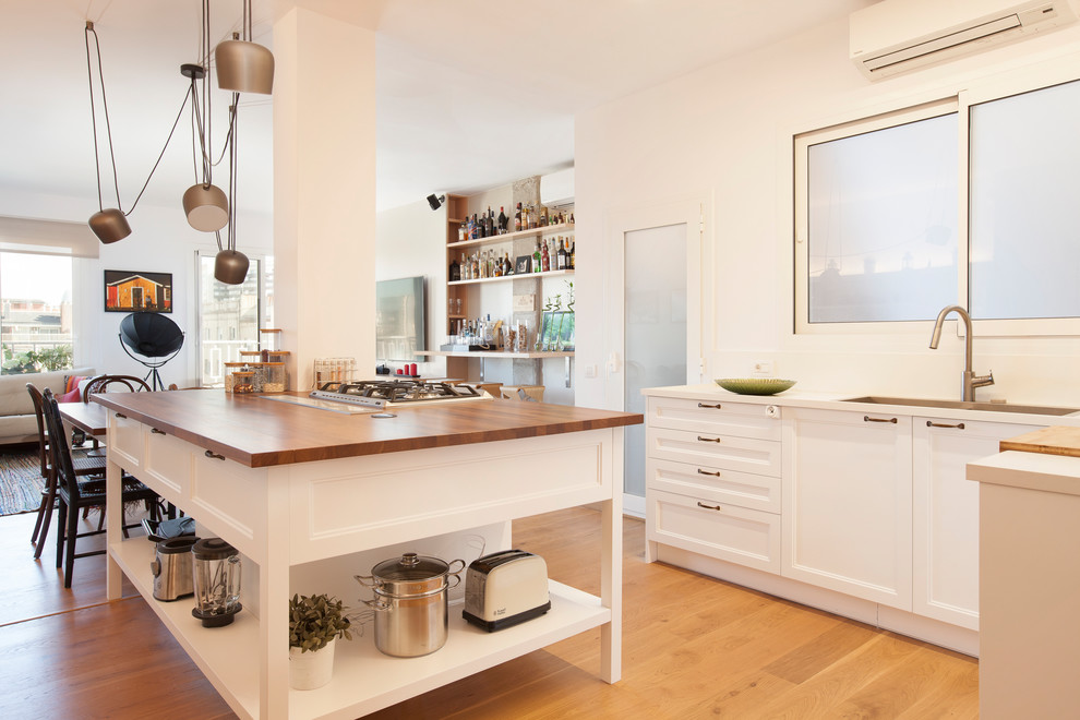 Diseño de cocina moderna grande abierta con armarios con paneles empotrados, puertas de armario blancas, encimera de madera, una isla y suelo marrón