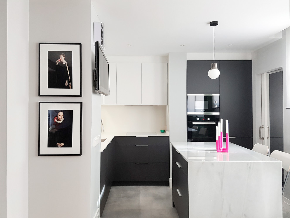 На фото: угловая кухня-гостиная среднего размера в современном стиле с врезной мойкой, плоскими фасадами, серыми фасадами, мраморной столешницей, белым фартуком, бетонным полом, островом, серым полом, черной техникой и телевизором с