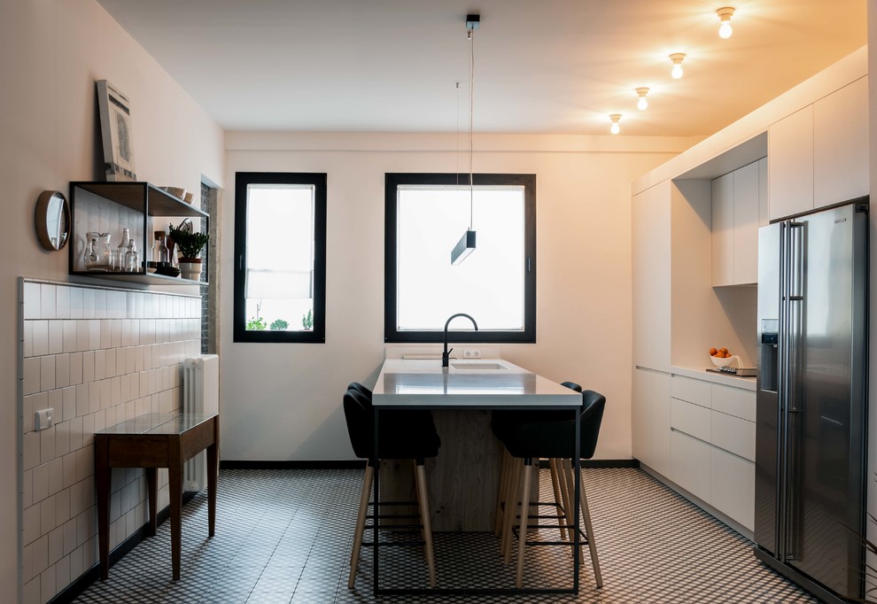 Свежая идея для дизайна: большая прямая кухня-гостиная в стиле неоклассика (современная классика) с плоскими фасадами, белыми фасадами, черной техникой, полом из керамической плитки, островом и разноцветным полом - отличное фото интерьера
