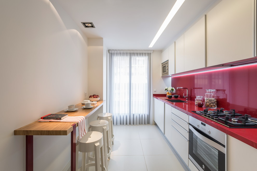 Foto på ett mellanstort funkis röd linjärt kök och matrum, med en enkel diskho, släta luckor, vita skåp, rött stänkskydd, rostfria vitvaror och klinkergolv i keramik