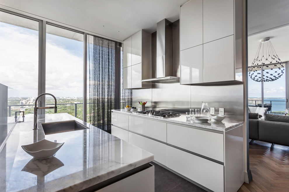 Zweizeilige Moderne Küche mit Unterbauwaschbecken, flächenbündigen Schrankfronten, weißen Schränken, Küchenrückwand in Metallic, Kücheninsel, grauem Boden und weißer Arbeitsplatte in Miami