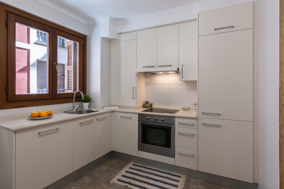 Imagen de cocinas en L contemporánea, sin isla, con fregadero encastrado, armarios con paneles lisos, puertas de armario blancas, salpicadero blanco, electrodomésticos con paneles, suelo gris y encimeras beige