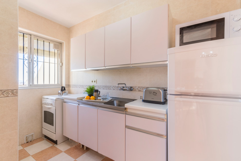 Small beach style single-wall enclosed kitchen in Other with a single-bowl sink, flat-panel cabinets, white cabinets, laminate countertops, beige splashback, ceramic splashback, white appliances, ceramic flooring, beige floors and white worktops.