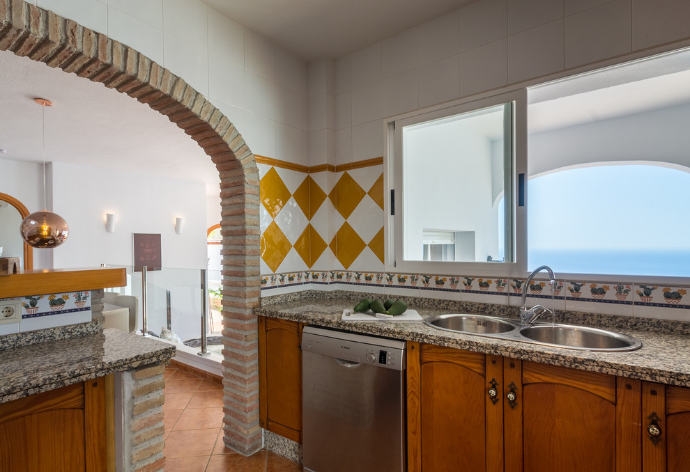 Example of a mid-sized tuscan l-shaped terra-cotta tile and brown floor open concept kitchen design in Other with a double-bowl sink, medium tone wood cabinets, granite countertops, multicolored backsplash, porcelain backsplash and stainless steel appliances