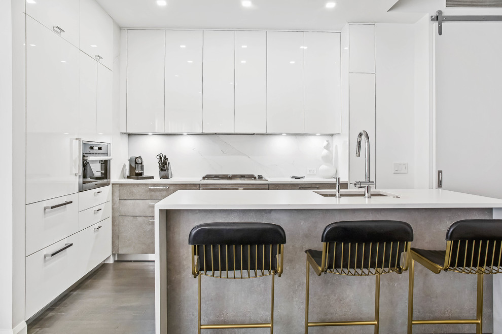 Modern inredning av ett mellanstort vit vitt l-kök, med bänkskiva i kvarts, en köksö, en undermonterad diskho, släta luckor, vita skåp, vitt stänkskydd, integrerade vitvaror, betonggolv och grått golv