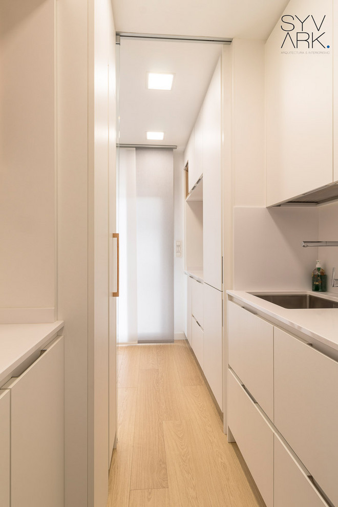 Esempio di una piccola cucina lineare minimalista chiusa con lavello sottopiano, ante lisce, ante bianche, top in quarzo composito, paraspruzzi bianco, elettrodomestici da incasso, pavimento in laminato, pavimento beige e top bianco