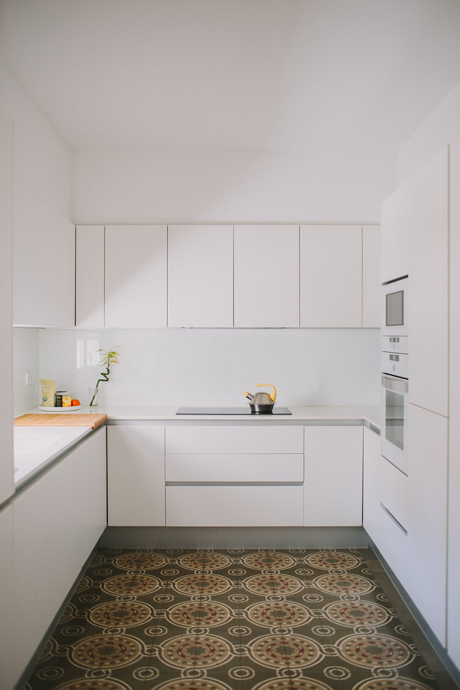 Modern inredning av ett litet vit vitt u-kök, med släta luckor, vita skåp, vitt stänkskydd och flerfärgat golv
