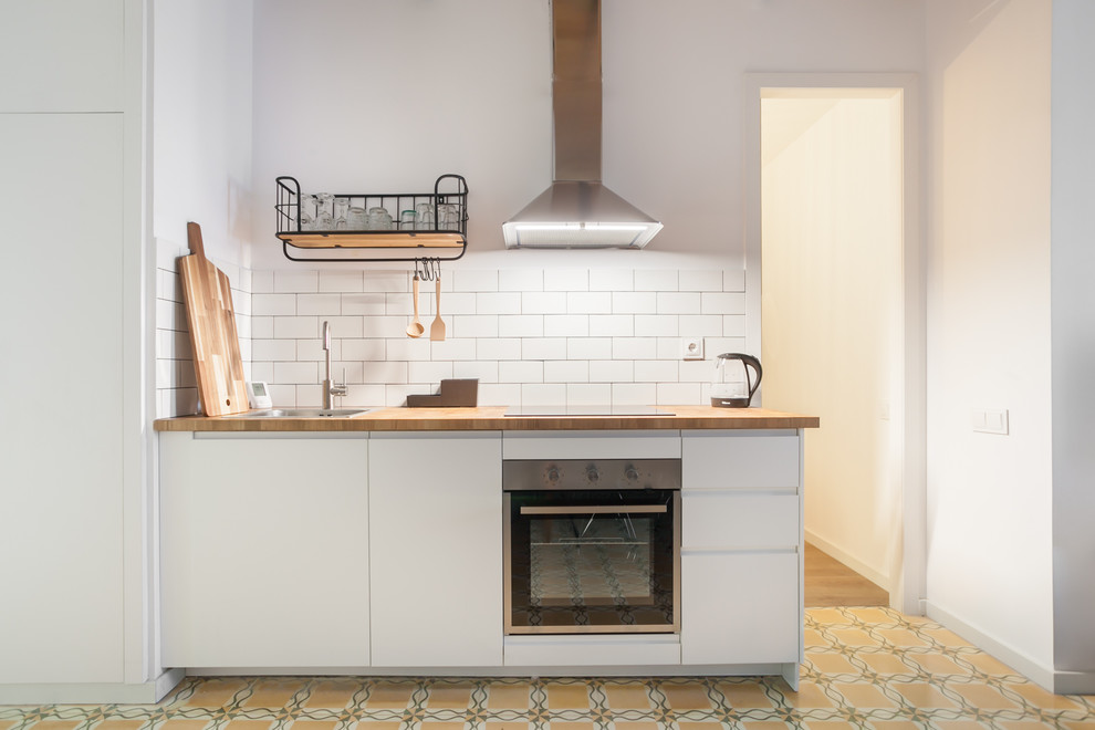 Immagine di una piccola cucina abitabile mediterranea con ante lisce, top in legno, elettrodomestici in acciaio inossidabile e pavimento giallo