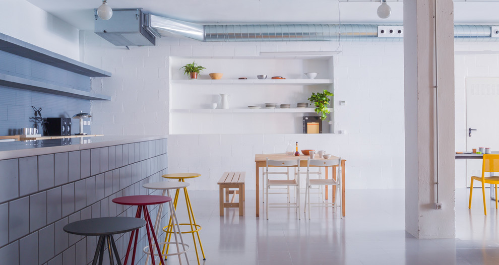 This is an example of a large industrial galley kitchen/diner in Barcelona with open cabinets, white cabinets, stainless steel worktops, blue splashback, stainless steel appliances, ceramic flooring and an island.
