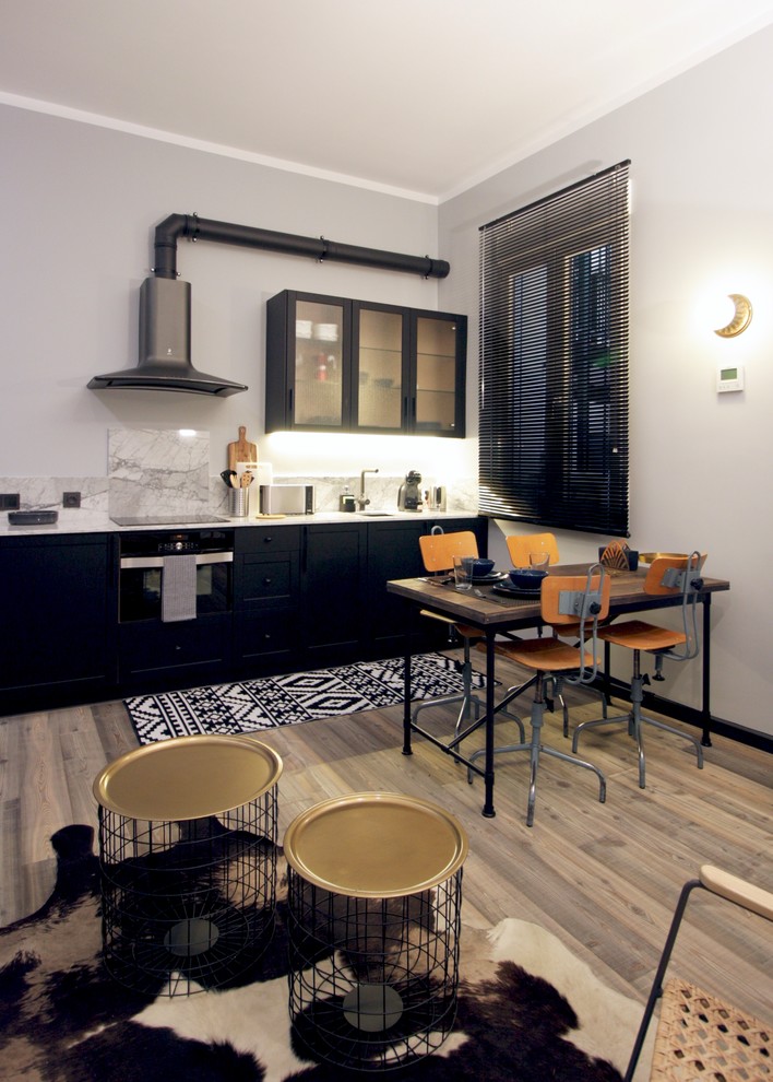 Cette image montre une cuisine ouverte linéaire urbaine avec des portes de placard noires, une crédence blanche, un électroménager noir, un plan de travail blanc, un placard à porte shaker, un sol en bois brun, aucun îlot et un sol marron.