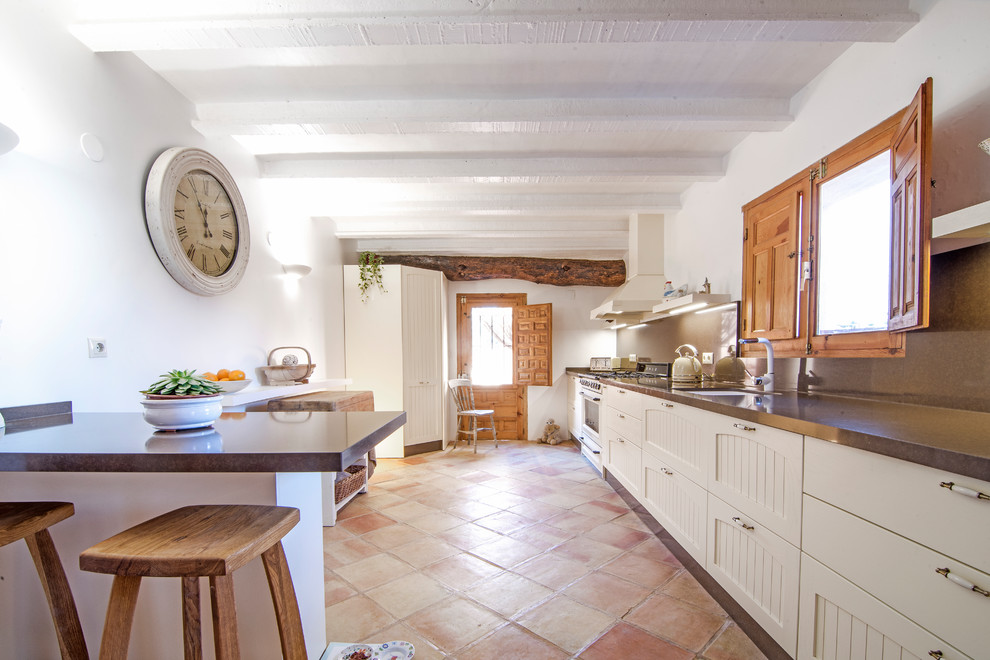 Réalisation d'une cuisine méditerranéenne en U fermée avec un évier encastré, un placard avec porte à panneau encastré, des portes de placard blanches, une crédence marron, un électroménager blanc, tomettes au sol, aucun îlot, un sol marron et un plan de travail marron.