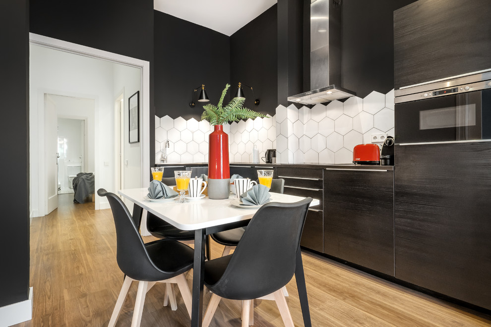 Inspiration for a medium sized contemporary l-shaped kitchen/diner in Barcelona with flat-panel cabinets, black cabinets, white splashback, ceramic splashback, black appliances, laminate floors, no island, stainless steel worktops, beige floors and grey worktops.