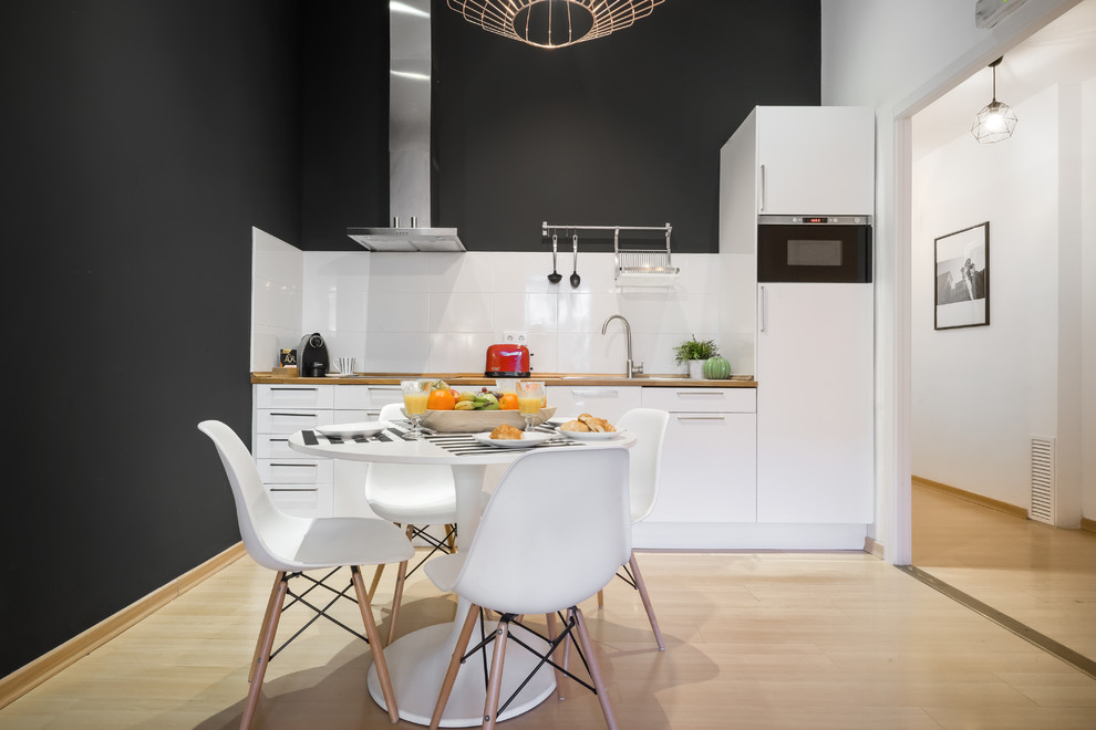 Eat-in kitchen - mid-sized contemporary single-wall light wood floor and beige floor eat-in kitchen idea in Barcelona with flat-panel cabinets, white cabinets, wood countertops, white backsplash, no island, brown countertops, a drop-in sink and paneled appliances