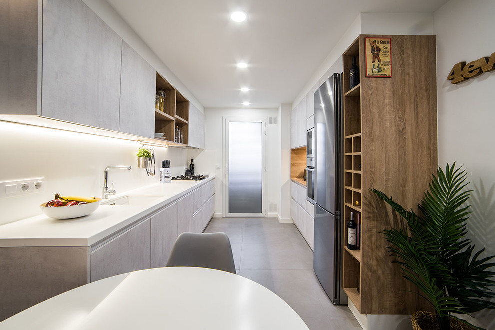 バルセロナにあるコンテンポラリースタイルのおしゃれなキッチン (フラットパネル扉のキャビネット、白いキッチンパネル、アイランドなし、白いキッチンカウンター、アンダーカウンターシンク、グレーのキャビネット、シルバーの調理設備、グレーの床) の写真