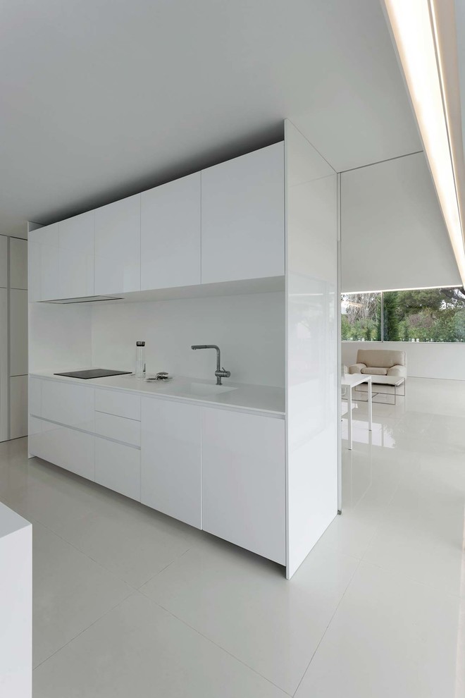 Идея дизайна: прямая кухня-гостиная в стиле модернизм с монолитной мойкой, плоскими фасадами, белыми фасадами, белым фартуком, белой столешницей, техникой под мебельный фасад и белым полом без острова