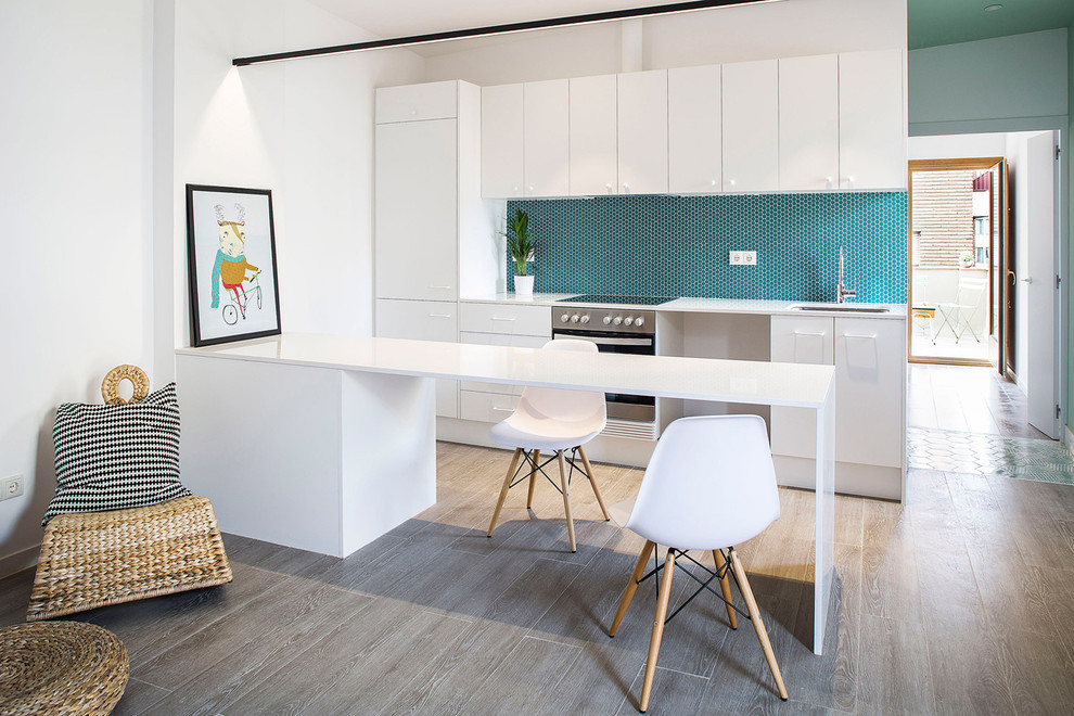 Immagine di una cucina minimal di medie dimensioni con lavello sottopiano, ante lisce, ante bianche, paraspruzzi blu, elettrodomestici in acciaio inossidabile, pavimento in legno massello medio e penisola