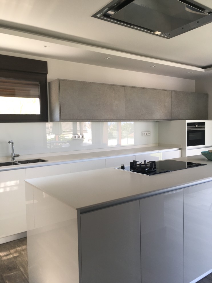 Example of a large minimalist u-shaped light wood floor and brown floor open concept kitchen design in Madrid with a double-bowl sink, flat-panel cabinets, white cabinets, quartz countertops, beige backsplash, window backsplash, stainless steel appliances, an island and white countertops