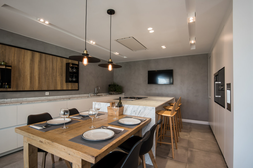 Zweizeilige Moderne Wohnküche mit flächenbündigen Schrankfronten, weißen Schränken, Marmor-Arbeitsplatte, Küchenrückwand in Grau, schwarzen Elektrogeräten und Halbinsel in Barcelona