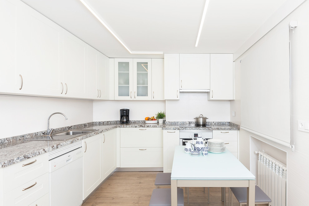 Inspiration for a medium sized contemporary l-shaped kitchen/diner in Madrid with a built-in sink, flat-panel cabinets, white cabinets, white appliances, light hardwood flooring, marble worktops, white splashback, no island and multicoloured worktops.