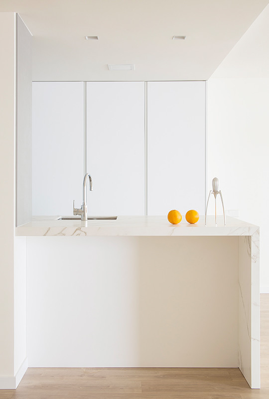 Cette image montre une grande cuisine américaine parallèle minimaliste avec un évier encastré, un placard à porte plane, des portes de placard blanches, un électroménager en acier inoxydable, sol en stratifié, une péninsule et un sol beige.