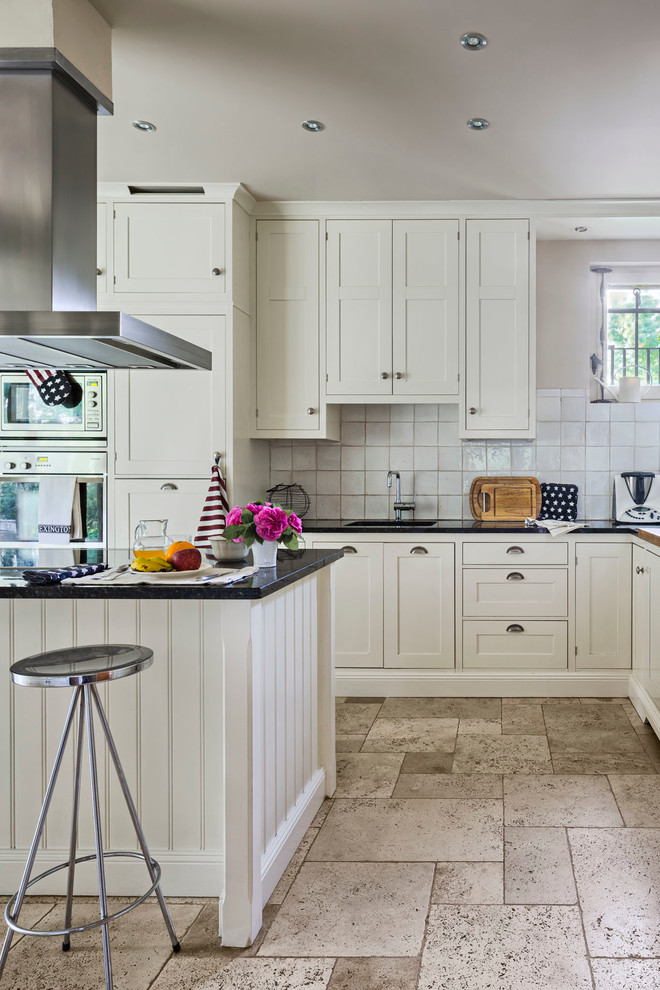 Inspiration for a large traditional u-shaped kitchen in Madrid with shaker cabinets, white cabinets, white splashback, stainless steel appliances, an island, a submerged sink, composite countertops, ceramic splashback and limestone flooring.