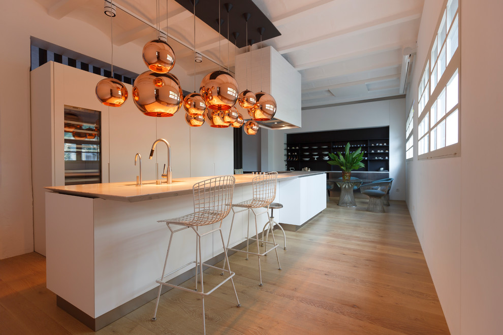 Large contemporary galley kitchen/diner in Palma de Mallorca with a submerged sink, flat-panel cabinets, white cabinets, stainless steel appliances, light hardwood flooring and an island.